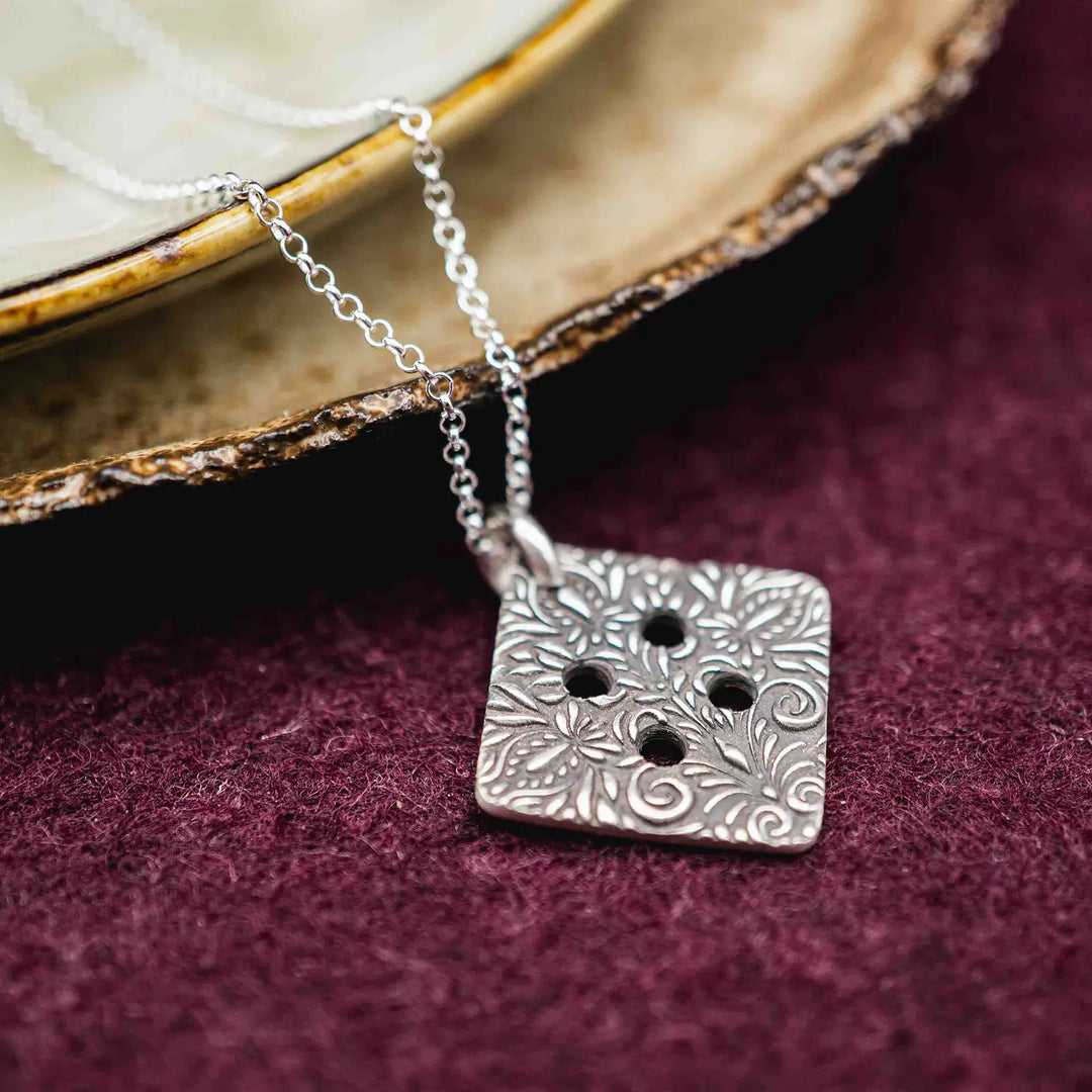 Freundschaftskette aus Silber 925 mit einem Knopf Anhänger an einer Kette. Der Knopf Anhänger ist eckig und mit einem floralen Muster versehen. Der eckige Knopf steht für Zusammenhalt, auch wenn nicht immer alles ganz "rund" läuft.