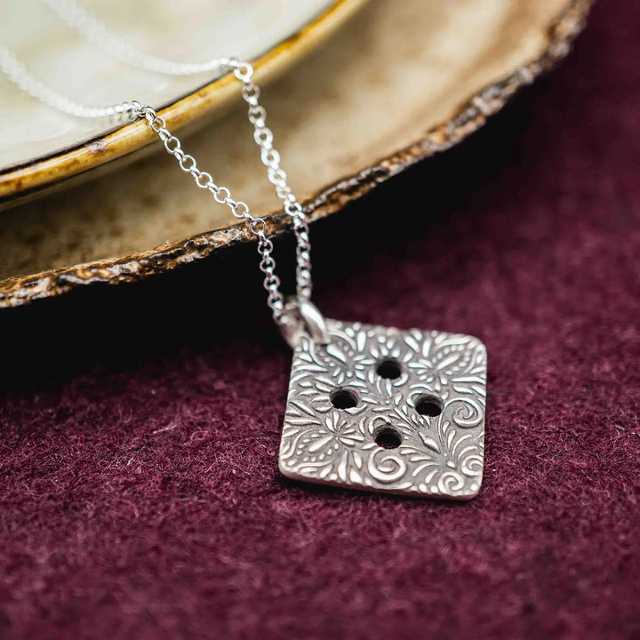 Freundschaftskette aus Silber 925 mit einem Knopf Anhänger an einer Kette. Der Knopf Anhänger ist eckig und mit einem floralen Muster versehen. Der eckige Knopf steht für Zusammenhalt, auch wenn nicht immer alles ganz "rund" läuft.