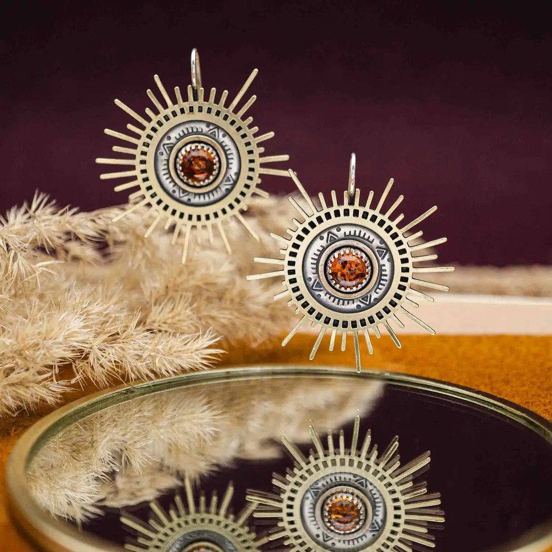 Große goldene Statement Ohrringe in Form einer Sonne mit Sonnenstrahlen. In der Mitte ist ein runder Bernstein in Sterling Silber 925 eingefasst. Die auffälligen und ausgefallenen Statement Ohrringe mit Goddess-Vibes sind handgefertigter Silberschmuck aus der Silberschmiede und bestehen aus Silber und goldenem Messing.