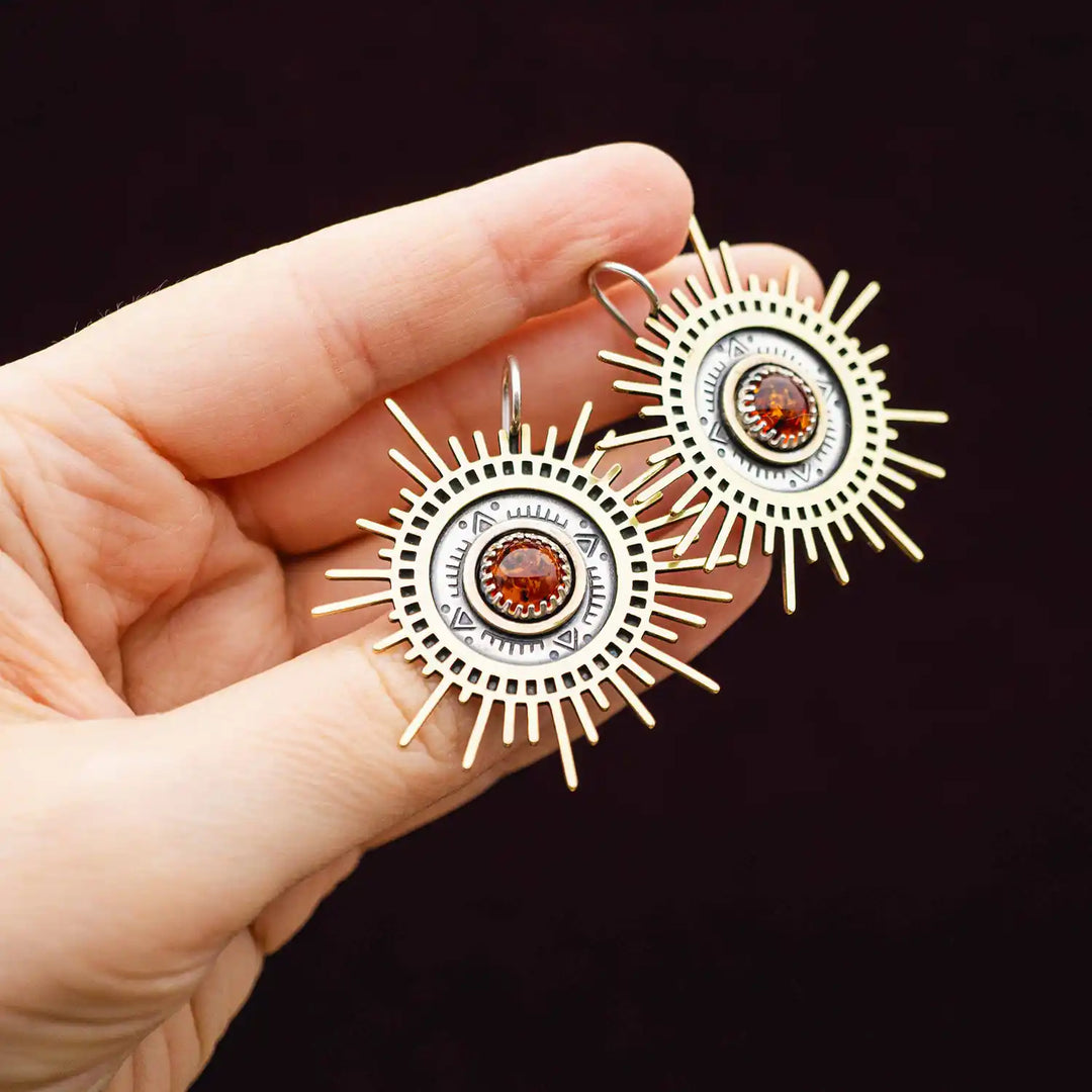 Große goldene Statement Ohrringe in Form einer Sonne mit Sonnenstrahlen. In der Mitte ist ein runder Bernstein in Sterling Silber 925 eingefasst. Die auffälligen und ausgefallenen Statement Ohrringe mit Goddess-Vibes sind handgefertigter Silberschmuck aus der Silberschmiede und bestehen aus Silber und goldenem Messing.