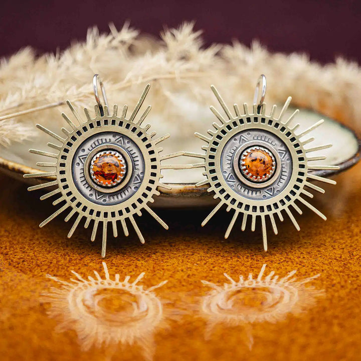 Große goldene Statement Ohrringe in Form einer Sonne mit Sonnenstrahlen. In der Mitte ist ein runder Bernstein in Sterling Silber 925 eingefasst. Die auffälligen und ausgefallenen Statement Ohrringe mit Goddess-Vibes sind handgefertigter Silberschmuck aus der Silberschmiede und bestehen aus Silber und goldenem Messing.