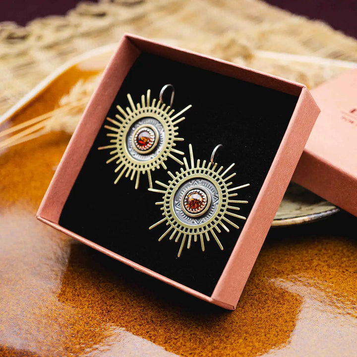 Große goldene Statement Ohrringe in Form einer Sonne mit Sonnenstrahlen. In der Mitte ist ein runder Bernstein in Sterling Silber 925 eingefasst. Die auffälligen und ausgefallenen Statement Ohrringe mit Goddess-Vibes sind handgefertigter Silberschmuck aus der Silberschmiede und bestehen aus Silber und goldenem Messing.