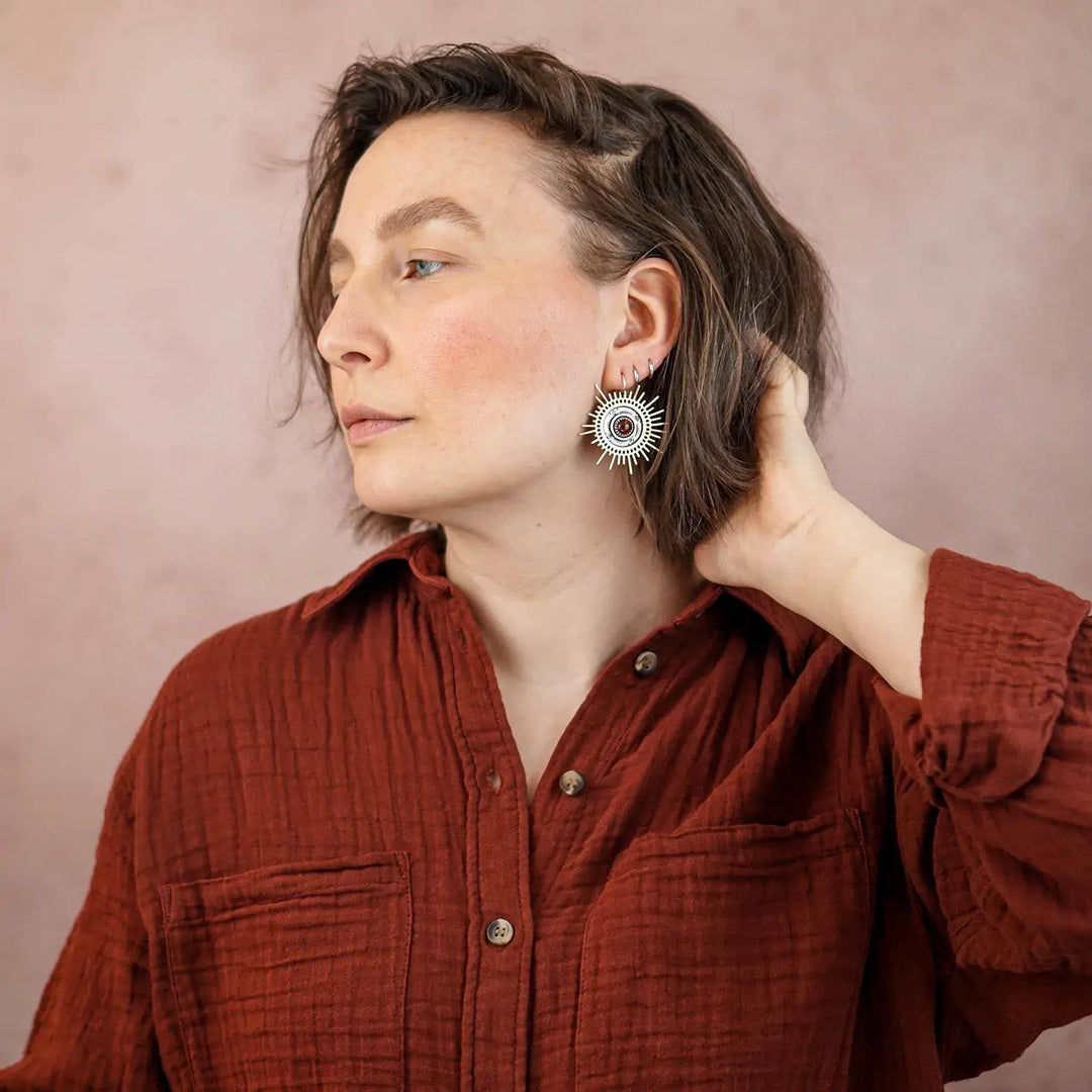 Große goldene Statement Ohrringe in Form einer Sonne mit Sonnenstrahlen. In der Mitte ist ein runder Bernstein in Sterling Silber 925 eingefasst. Die auffälligen und ausgefallenen Statement Ohrringe mit Goddess-Vibes sind handgefertigter Silberschmuck aus der Silberschmiede und bestehen aus Silber und goldenem Messing.