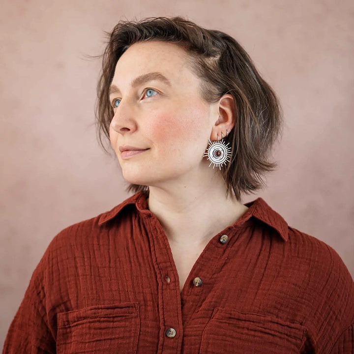 Große goldene Statement Ohrringe in Form einer Sonne mit Sonnenstrahlen. In der Mitte ist ein runder Bernstein in Sterling Silber 925 eingefasst. Die auffälligen und ausgefallenen Statement Ohrringe mit Goddess-Vibes sind handgefertigter Silberschmuck aus der Silberschmiede und bestehen aus Silber und goldenem Messing.