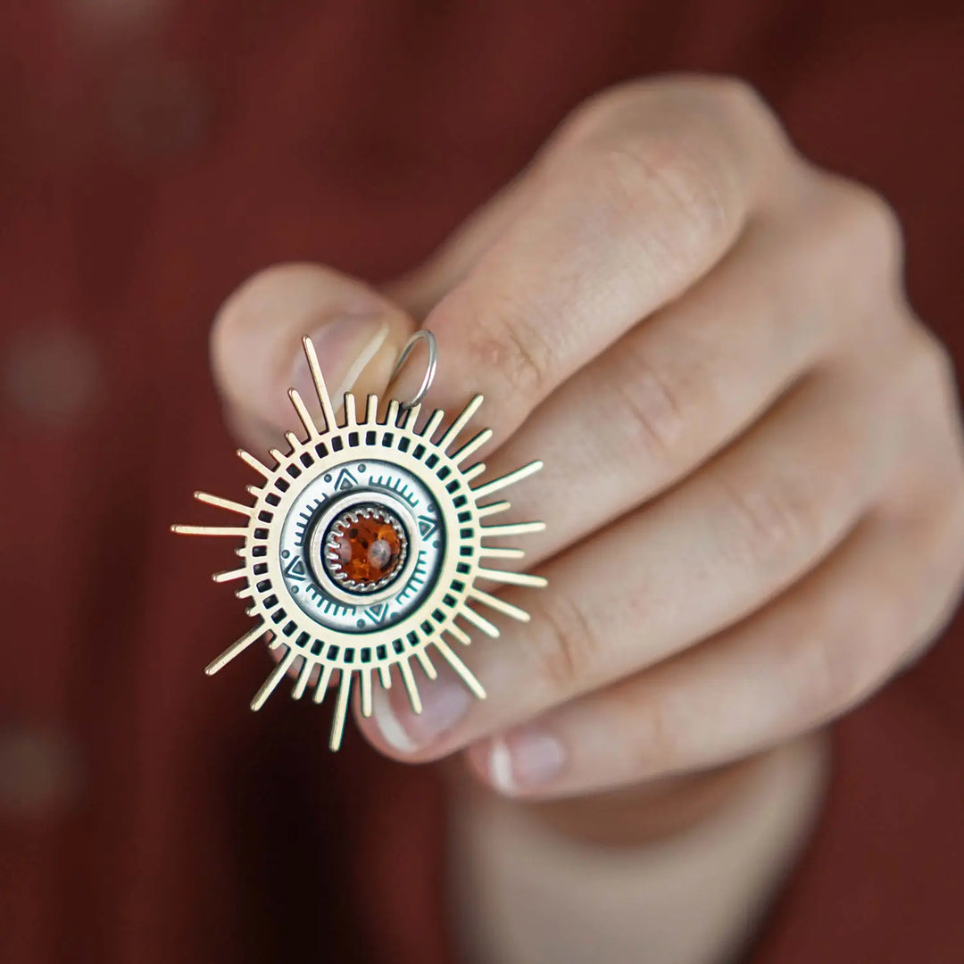 Große goldene Statement Ohrringe in Form einer Sonne mit Sonnenstrahlen. In der Mitte ist ein runder Bernstein in Sterling Silber 925 eingefasst. Die auffälligen und ausgefallenen Statement Ohrringe mit Goddess-Vibes sind handgefertigter Silberschmuck aus der Silberschmiede und bestehen aus Silber und goldenem Messing.