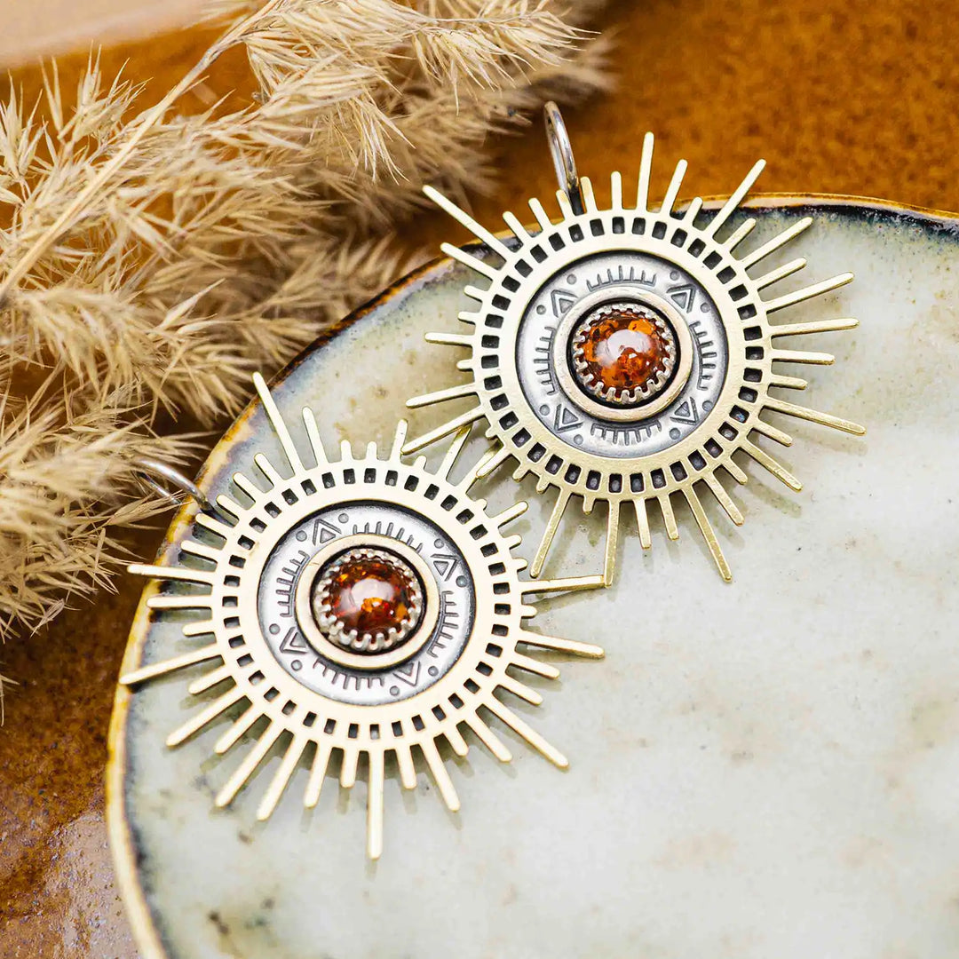 Große goldene Statement Ohrringe in Form einer Sonne mit Sonnenstrahlen. In der Mitte ist ein runder Bernstein in Sterling Silber 925 eingefasst. Die auffälligen und ausgefallenen Statement Ohrringe mit Goddess-Vibes sind handgefertigter Silberschmuck aus der Silberschmiede und bestehen aus Silber und goldenem Messing.