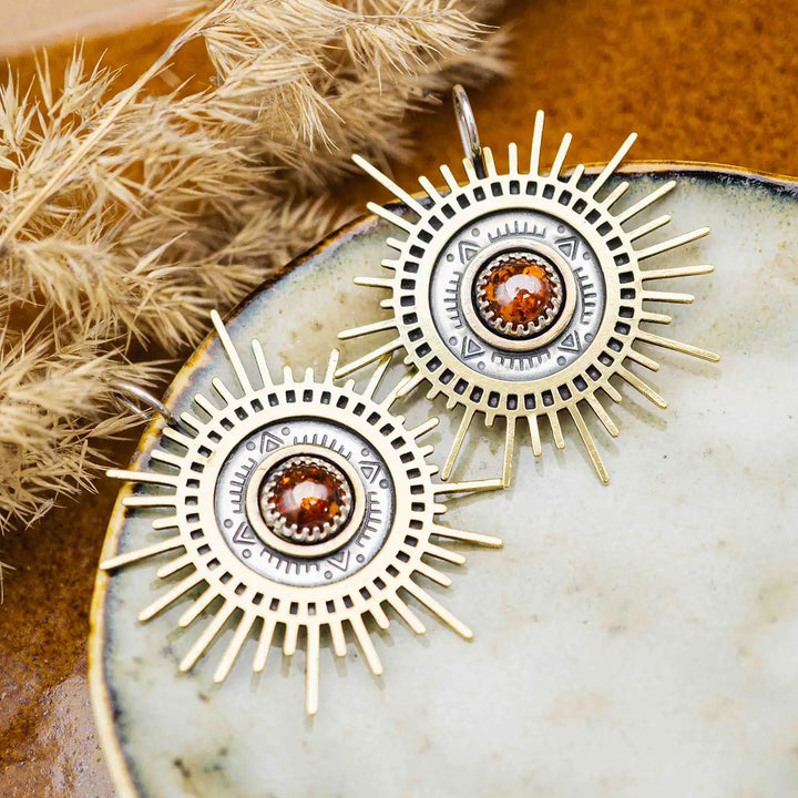Große goldene Statement Ohrringe in Form einer Sonne mit Sonnenstrahlen. In der Mitte ist ein runder Bernstein in Sterling Silber 925 eingefasst. Die auffälligen und ausgefallenen Statement Ohrringe mit Goddess-Vibes sind handgefertigter Silberschmuck aus der Silberschmiede und bestehen aus Silber und goldenem Messing.