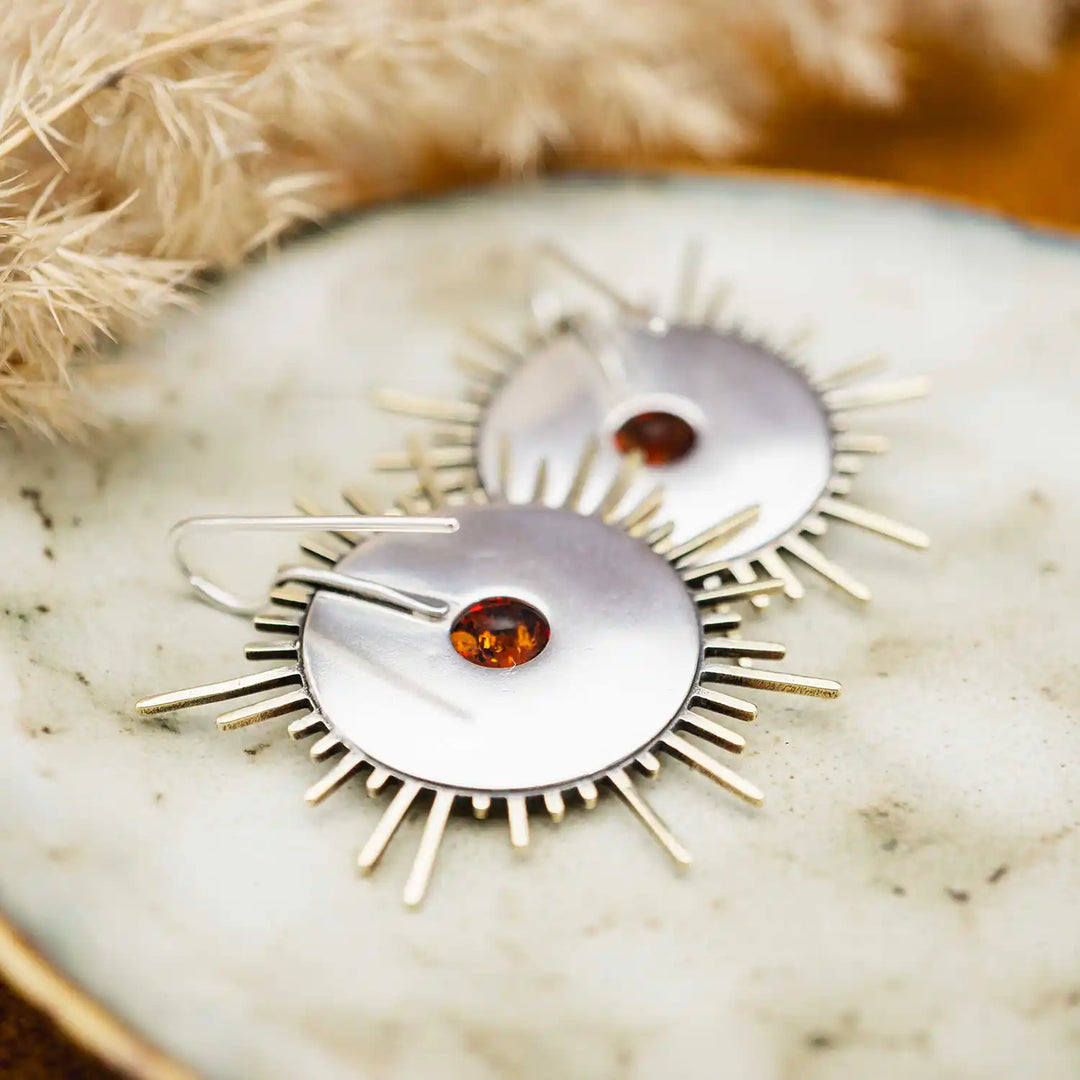 Große goldene Statement Ohrringe in Form einer Sonne mit Sonnenstrahlen. In der Mitte ist ein runder Bernstein in Sterling Silber 925 eingefasst. Die auffälligen und ausgefallenen Statement Ohrringe mit Goddess-Vibes sind handgefertigter Silberschmuck aus der Silberschmiede und bestehen aus Silber und goldenem Messing.