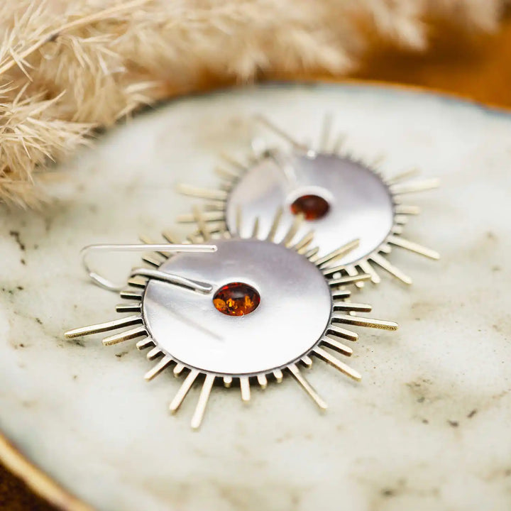 Große goldene Statement Ohrringe in Form einer Sonne mit Sonnenstrahlen. In der Mitte ist ein runder Bernstein in Sterling Silber 925 eingefasst. Die auffälligen und ausgefallenen Statement Ohrringe mit Goddess-Vibes sind handgefertigter Silberschmuck aus der Silberschmiede und bestehen aus Silber und goldenem Messing.