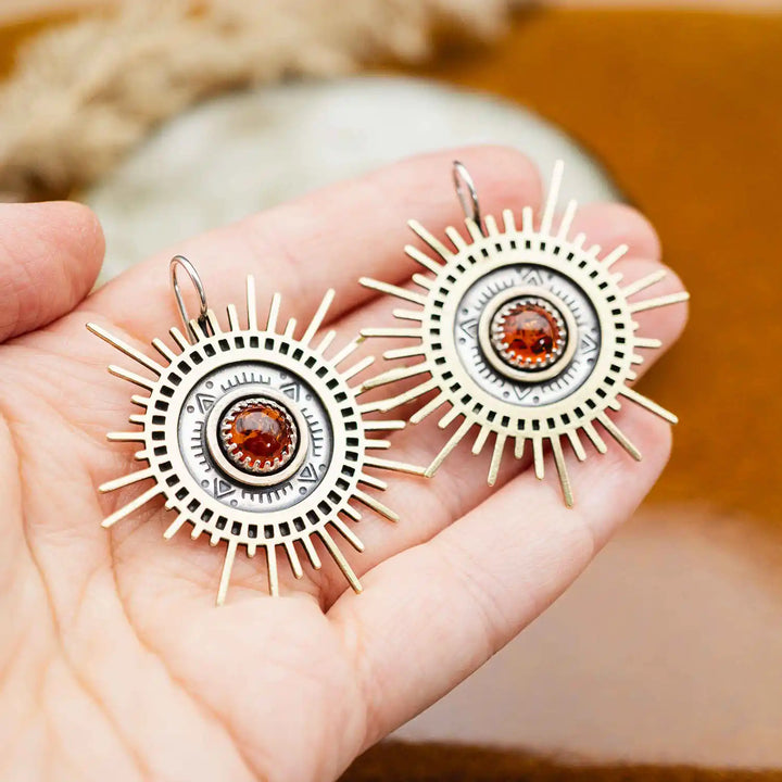 Große goldene Statement Ohrringe in Form einer Sonne mit Sonnenstrahlen. In der Mitte ist ein runder Bernstein in Sterling Silber 925 eingefasst. Die auffälligen und ausgefallenen Statement Ohrringe mit Goddess-Vibes sind handgefertigter Silberschmuck aus der Silberschmiede und bestehen aus Silber und goldenem Messing.