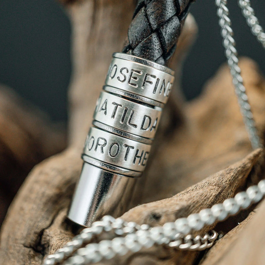 Eine Halskette für Männer aus braunem Leder-Anhänger und einer Edelstahl-Kette. Die Kette für Herren ist an dem zylindrischen Anhänger aus Leder personalisiert mit Gravur von Namen oder Datum auf zylindrischen Sterling Silber 925 Perlen. Die Kette lässt sich mit einem silbernen Karabiner aus Edelstahl verschließen.