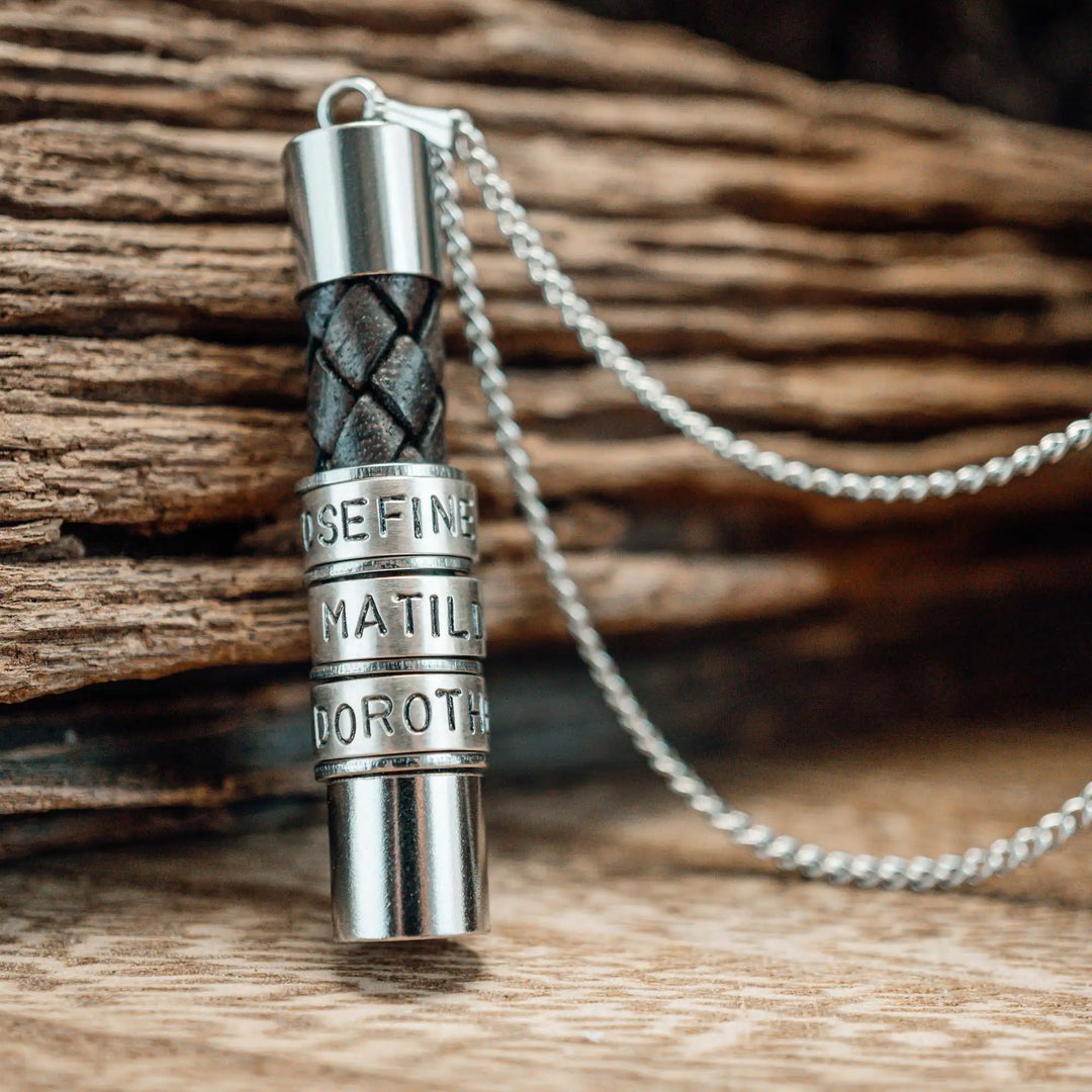 Eine Halskette für Männer aus braunem Leder-Anhänger und einer Edelstahl-Kette. Die Kette für Herren ist an dem zylindrischen Anhänger aus Leder personalisiert mit Gravur von Namen oder Datum auf zylindrischen Sterling Silber 925 Perlen. Die Kette lässt sich mit einem silbernen Karabiner aus Edelstahl verschließen.
