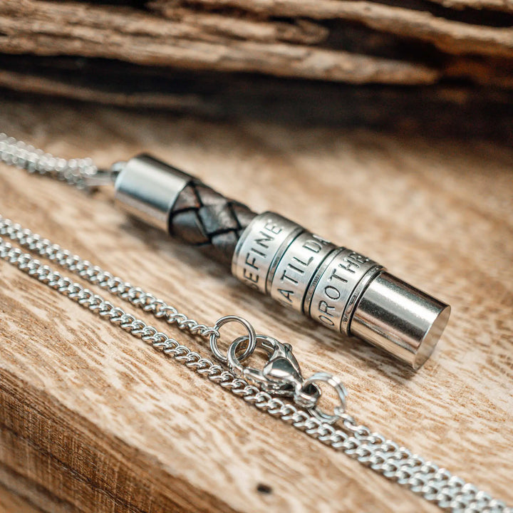Eine Halskette für Männer aus braunem Leder-Anhänger und einer Edelstahl-Kette. Die Kette für Herren ist an dem zylindrischen Anhänger aus Leder personalisiert mit Gravur von Namen oder Datum auf zylindrischen Sterling Silber 925 Perlen. Die Kette lässt sich mit einem silbernen Karabiner aus Edelstahl verschließen.