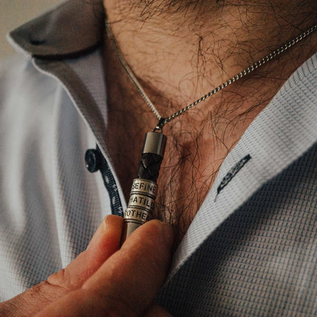 Eine Halskette für Männer aus braunem Leder-Anhänger und einer Edelstahl-Kette. Die Kette für Herren ist an dem zylindrischen Anhänger aus Leder personalisiert mit Gravur von Namen oder Datum auf zylindrischen Sterling Silber 925 Perlen. Die Kette lässt sich mit einem silbernen Karabiner aus Edelstahl verschließen.
