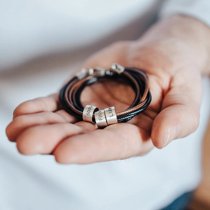 Eine vegane Halskette für Männer aus mehreren braunen und schwarzen Synthetik/Baumwoll-Bändern. Die Kette für Herren ist personalisiert mit Gravur von Namen oder Datum auf zylindrischen Sterling Silber 925 Perlen. Das Kette lässt sich mit einem stabilen Karabiner Verschluss aus Edelstahl verschließen.
