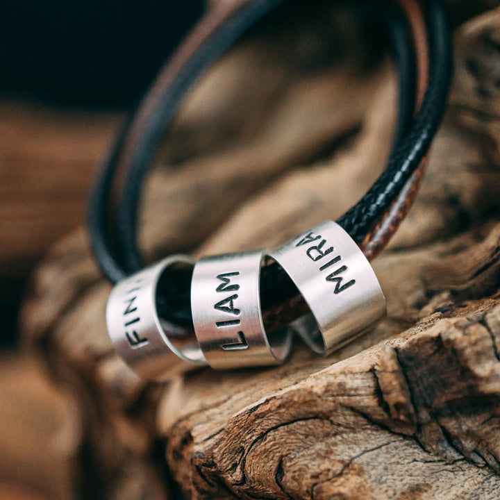 Eine vegane Halskette für Männer aus mehreren braunen und schwarzen Synthetik/Baumwoll-Bändern. Die Kette für Herren ist personalisiert mit Gravur von Namen oder Datum auf zylindrischen Sterling Silber 925 Perlen. Das Kette lässt sich mit einem stabilen Karabiner Verschluss aus Edelstahl verschließen.