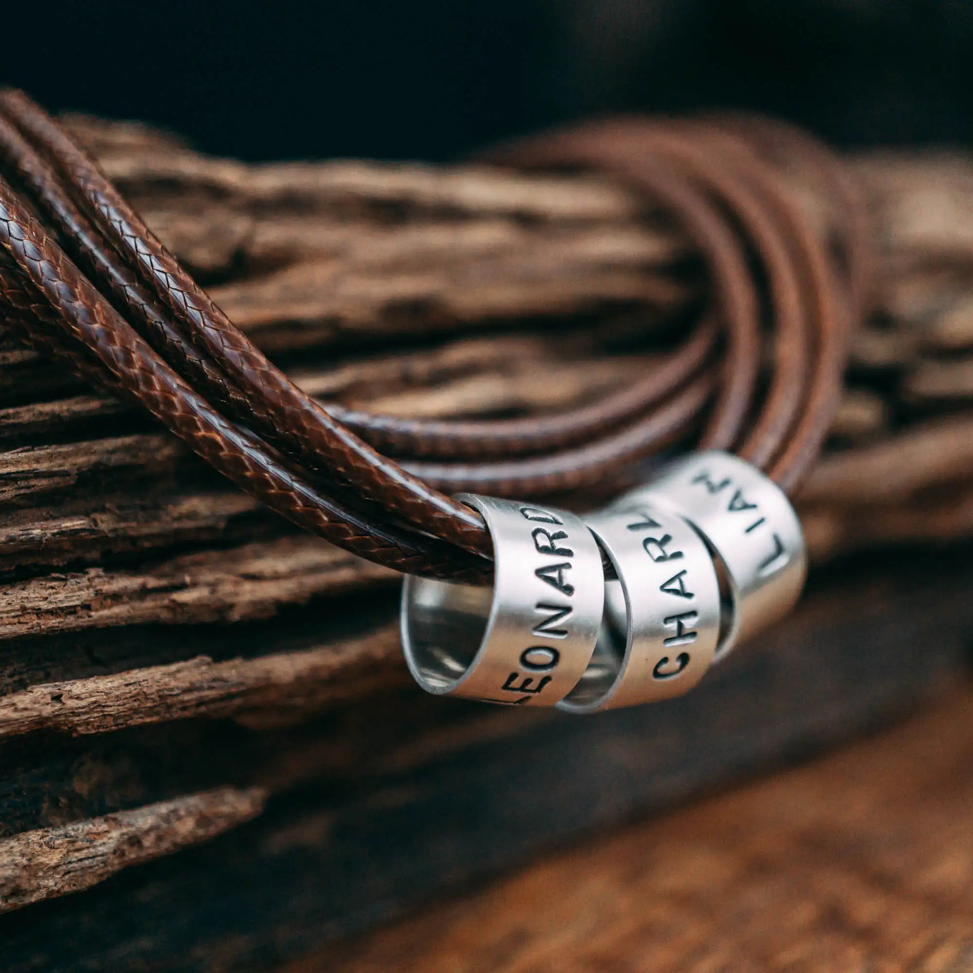 Eine vegane Halskette für Männer aus mehreren braunen Synthetik/Baumwoll-Bändern. Die Kette für Herren ist personalisiert mit Gravur von Namen oder Datum auf zylindrischen Sterling Silber 925 Perlen. Das Kette lässt sich mit einem stabilen Karabiner Verschluss aus Edelstahl verschließen.