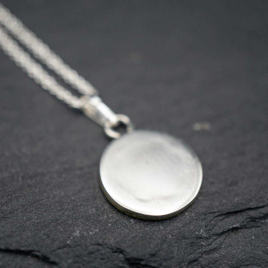 Zarte Kette aus Sterling Silber 925 und rundem Anhänger mit goldener Biene. Die Kette ist schwarz patiniert und mit einem goldenen Rahmen aus Messing verziert.