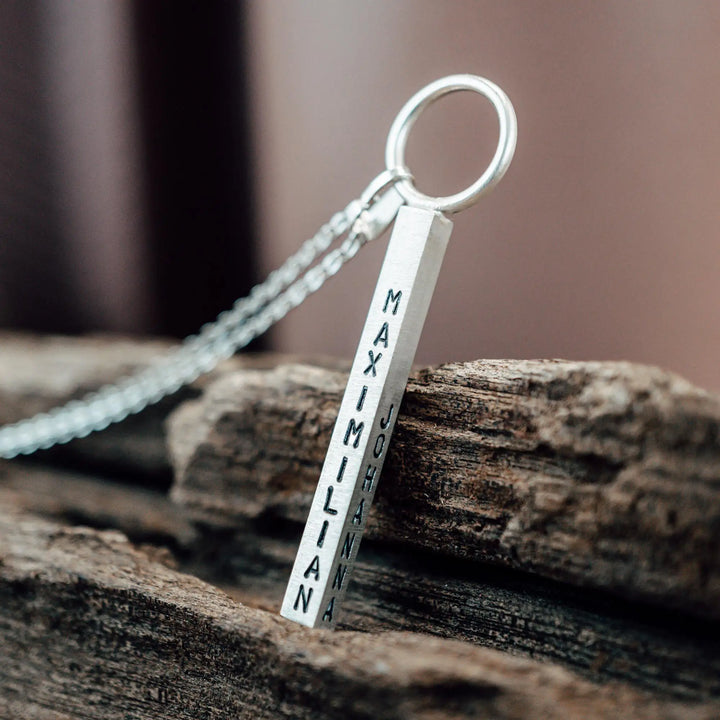 Eine Halskette mit Gravur für Frauen. Sie besteht aus einem Anhänger an einem Ring und einer Kette aus Sterling Silber 925. Die Kette für Damen ist auf dem ca 4cm langen, rechteckigen Anhänger personalisiert mit Gravur von Namen oder Datum auf allen 4 Seiten des Anhängers. Die Kette lässt sich mit einem silbernen Karabiner aus Edelstahl verschließen.