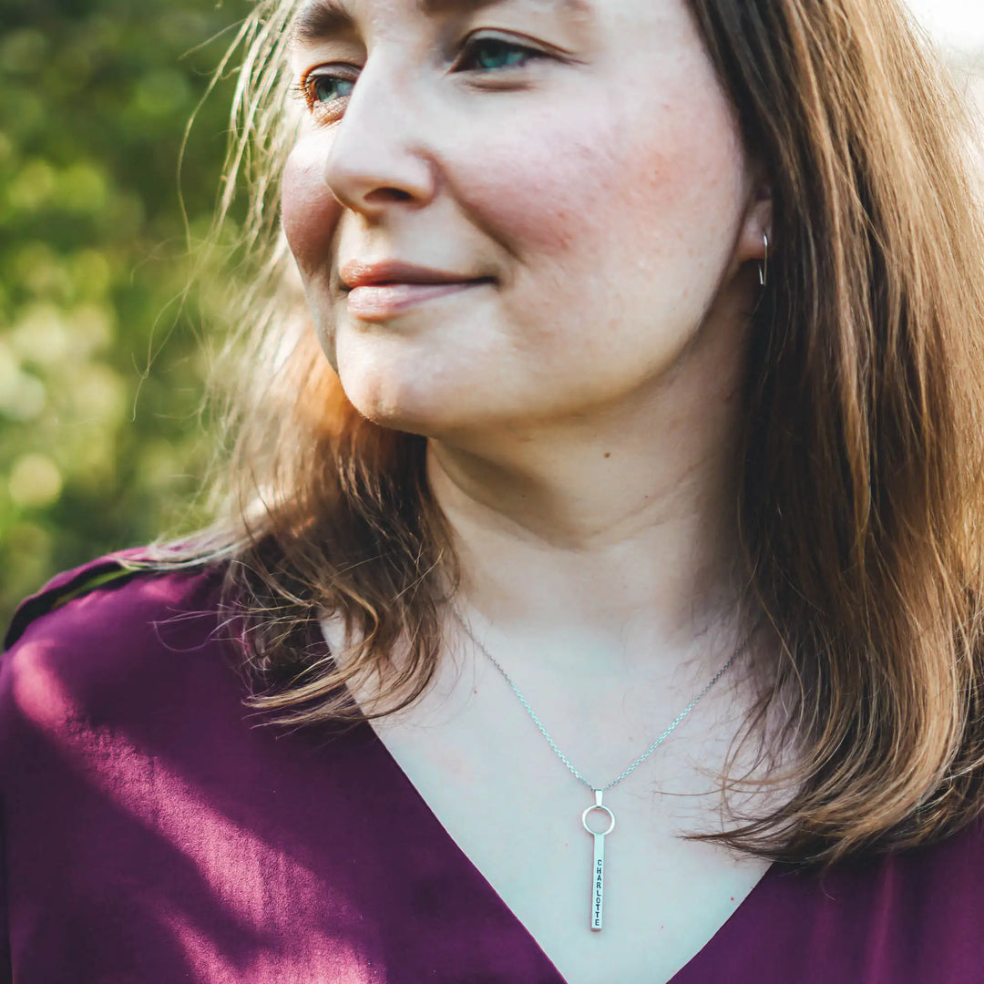 Eine Halskette mit Gravur für Frauen. Sie besteht aus einem Anhänger an einem Ring und einer Kette aus Sterling Silber 925. Die Kette für Damen ist auf dem ca 4cm langen, rechteckigen Anhänger personalisiert mit Gravur von Namen oder Datum auf allen 4 Seiten des Anhängers. Die Kette lässt sich mit einem silbernen Karabiner aus Edelstahl verschließen.