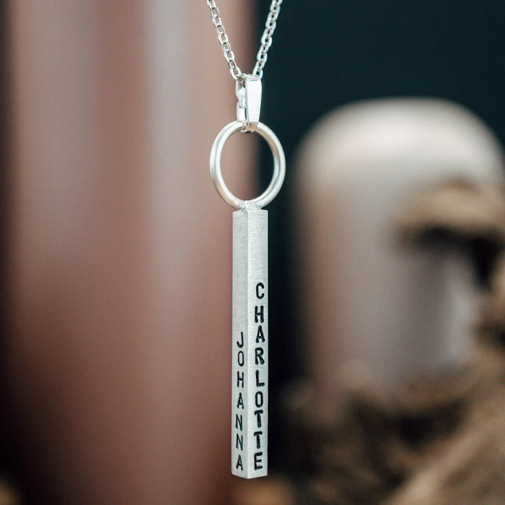 Eine Halskette mit Gravur für Frauen. Sie besteht aus einem Anhänger an einem Ring und einer Kette aus Sterling Silber 925. Die Kette für Damen ist auf dem ca 4cm langen, rechteckigen Anhänger personalisiert mit Gravur von Namen oder Datum auf allen 4 Seiten des Anhängers. Die Kette lässt sich mit einem silbernen Karabiner aus Edelstahl verschließen.