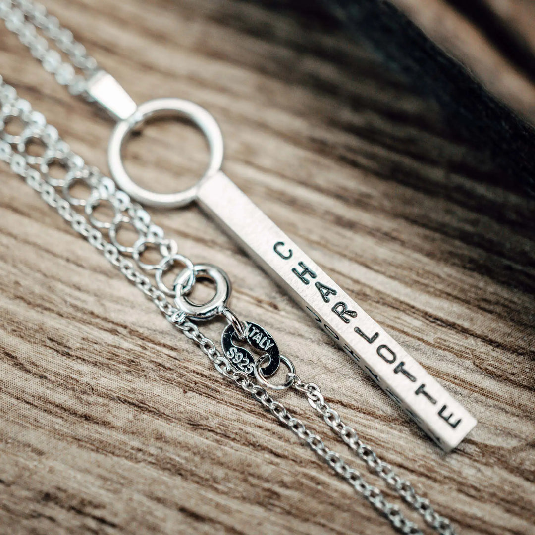 Eine Halskette mit Gravur für Frauen. Sie besteht aus einem Anhänger an einem Ring und einer Kette aus Sterling Silber 925. Die Kette für Damen ist auf dem ca 4cm langen, rechteckigen Anhänger personalisiert mit Gravur von Namen oder Datum auf allen 4 Seiten des Anhängers. Die Kette lässt sich mit einem silbernen Karabiner aus Edelstahl verschließen.