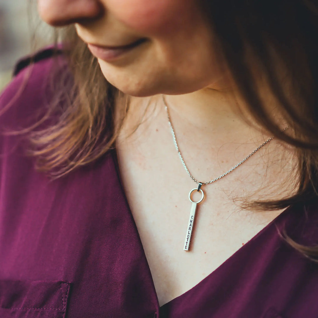 Eine Halskette mit Gravur für Frauen. Sie besteht aus einem Anhänger an einem Ring und einer Kette aus Sterling Silber 925. Die Kette für Damen ist auf dem ca 4cm langen, rechteckigen Anhänger personalisiert mit Gravur von Namen oder Datum auf allen 4 Seiten des Anhängers. Die Kette lässt sich mit einem silbernen Karabiner aus Edelstahl verschließen.