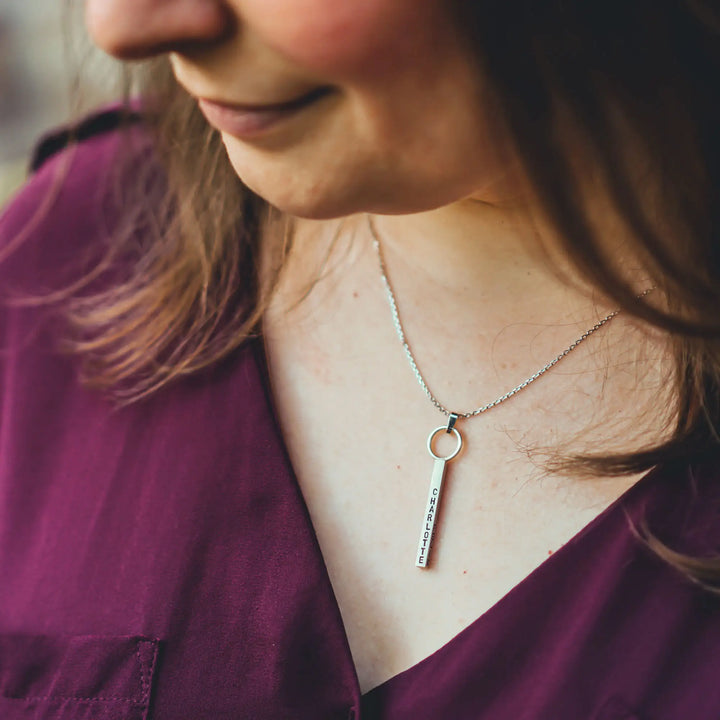 Eine Halskette mit Gravur für Frauen. Sie besteht aus einem Anhänger an einem Ring und einer Kette aus Sterling Silber 925. Die Kette für Damen ist auf dem ca 4cm langen, rechteckigen Anhänger personalisiert mit Gravur von Namen oder Datum auf allen 4 Seiten des Anhängers. Die Kette lässt sich mit einem silbernen Karabiner aus Edelstahl verschließen.