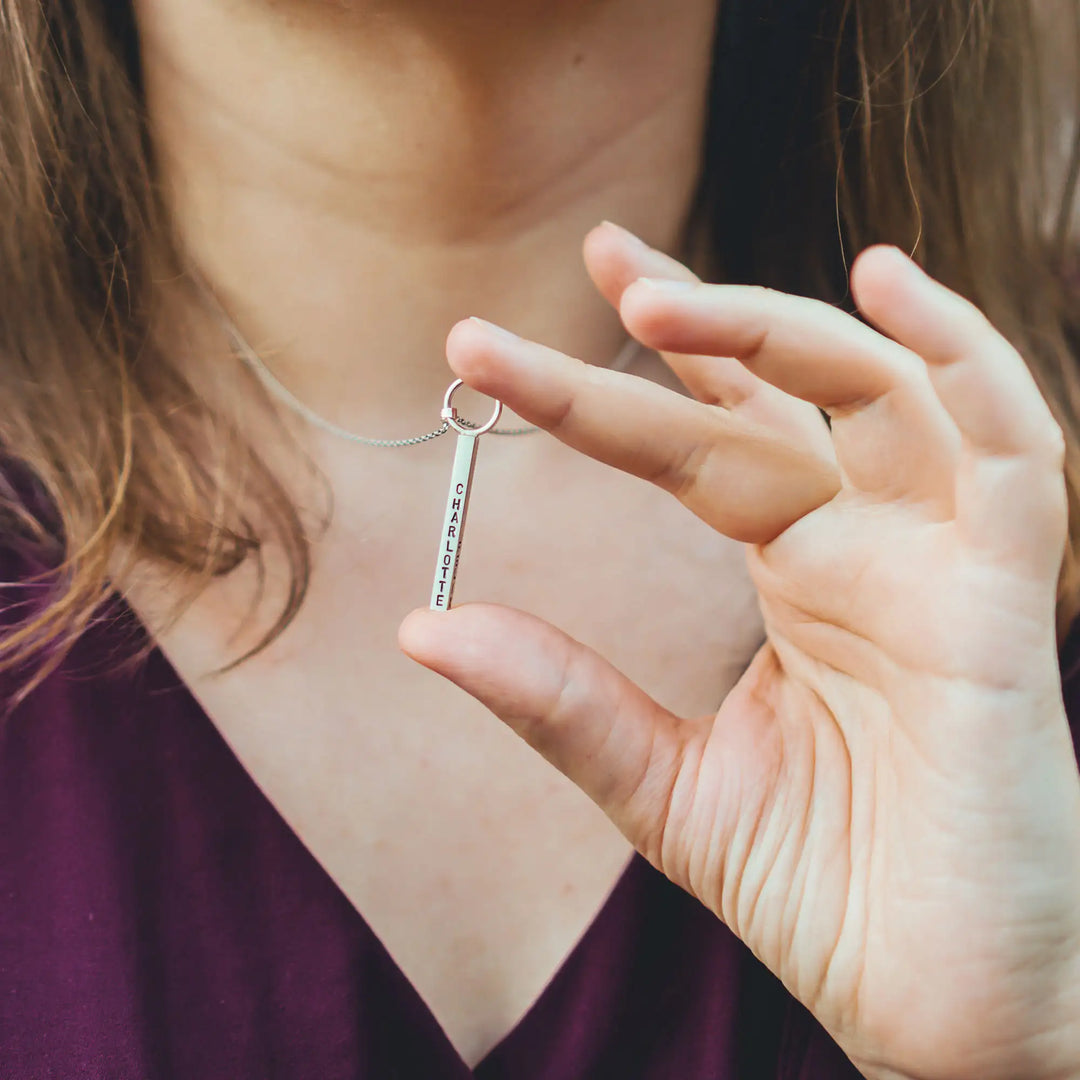 Eine Halskette mit Gravur für Frauen. Sie besteht aus einem Anhänger an einem Ring und einer Kette aus Sterling Silber 925. Die Kette für Damen ist auf dem ca 4cm langen, rechteckigen Anhänger personalisiert mit Gravur von Namen oder Datum auf allen 4 Seiten des Anhängers. Die Kette lässt sich mit einem silbernen Karabiner aus Edelstahl verschließen.