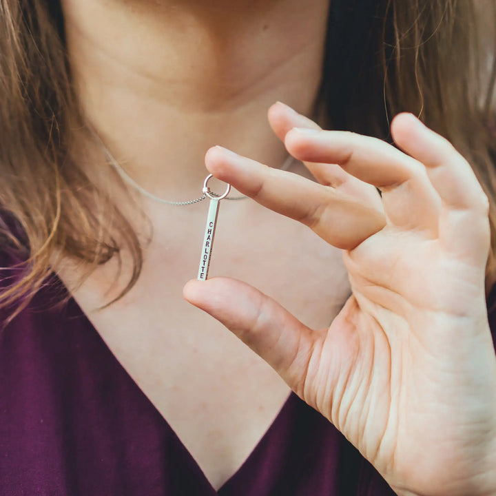 Eine Halskette mit Gravur für Frauen. Sie besteht aus einem Anhänger an einem Ring und einer Kette aus Sterling Silber 925. Die Kette für Damen ist auf dem ca 4cm langen, rechteckigen Anhänger personalisiert mit Gravur von Namen oder Datum auf allen 4 Seiten des Anhängers. Die Kette lässt sich mit einem silbernen Karabiner aus Edelstahl verschließen.