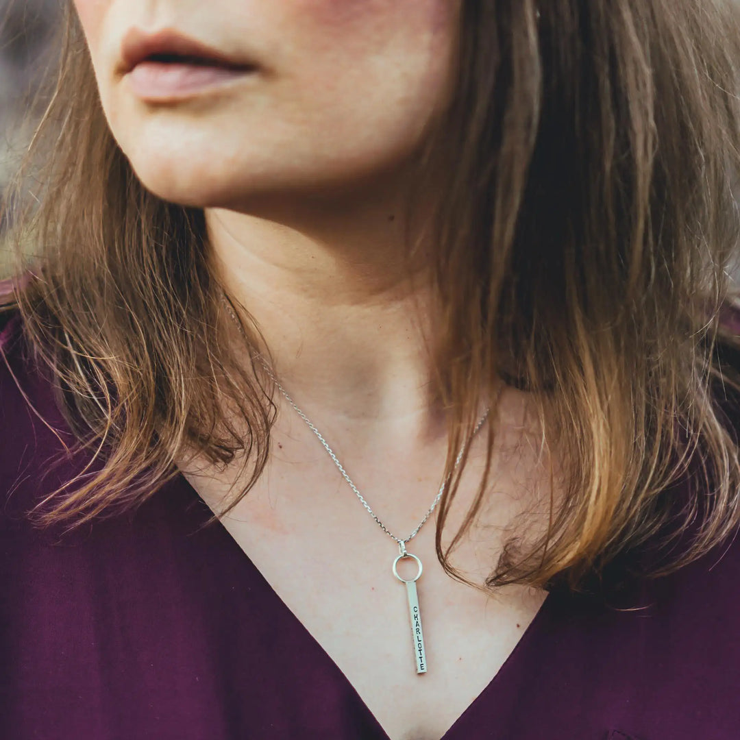 Eine Halskette mit Gravur für Frauen. Sie besteht aus einem Anhänger an einem Ring und einer Kette aus Sterling Silber 925. Die Kette für Damen ist auf dem ca 4cm langen, rechteckigen Anhänger personalisiert mit Gravur von Namen oder Datum auf allen 4 Seiten des Anhängers. Die Kette lässt sich mit einem silbernen Karabiner aus Edelstahl verschließen.