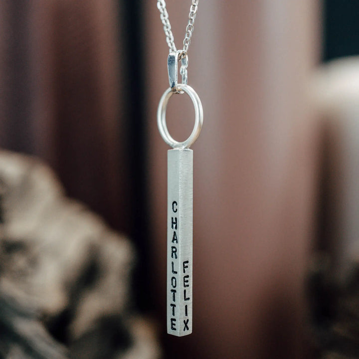 Eine Halskette mit Gravur für Frauen. Sie besteht aus einem Anhänger an einem Ring und einer Kette aus Sterling Silber 925. Die Kette für Damen ist auf dem ca 4cm langen, rechteckigen Anhänger personalisiert mit Gravur von Namen oder Datum auf allen 4 Seiten des Anhängers. Die Kette lässt sich mit einem silbernen Karabiner aus Edelstahl verschließen.
