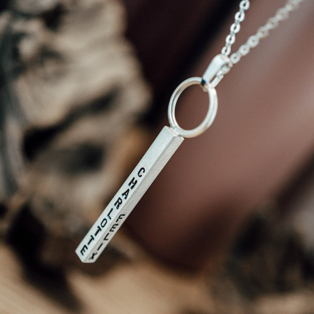 Eine Halskette mit Gravur für Frauen. Sie besteht aus einem Anhänger an einem Ring und einer Kette aus Sterling Silber 925. Die Kette für Damen ist auf dem ca 4cm langen, rechteckigen Anhänger personalisiert mit Gravur von Namen oder Datum auf allen 4 Seiten des Anhängers. Die Kette lässt sich mit einem silbernen Karabiner aus Edelstahl verschließen.