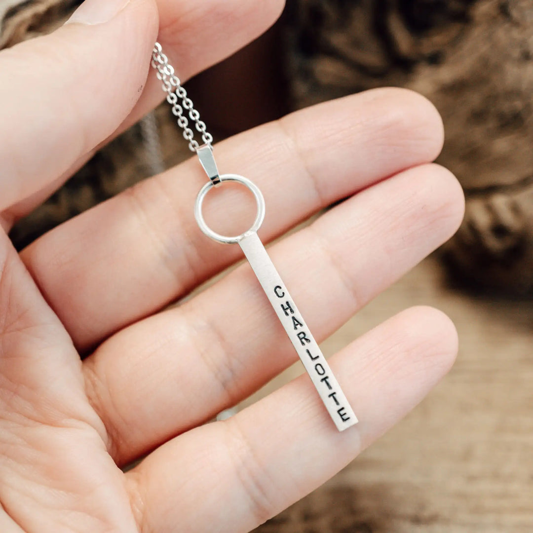 Eine Halskette mit Gravur für Frauen. Sie besteht aus einem Anhänger an einem Ring und einer Kette aus Sterling Silber 925. Die Kette für Damen ist auf dem ca 4cm langen, rechteckigen Anhänger personalisiert mit Gravur von Namen oder Datum auf allen 4 Seiten des Anhängers. Die Kette lässt sich mit einem silbernen Karabiner aus Edelstahl verschließen.