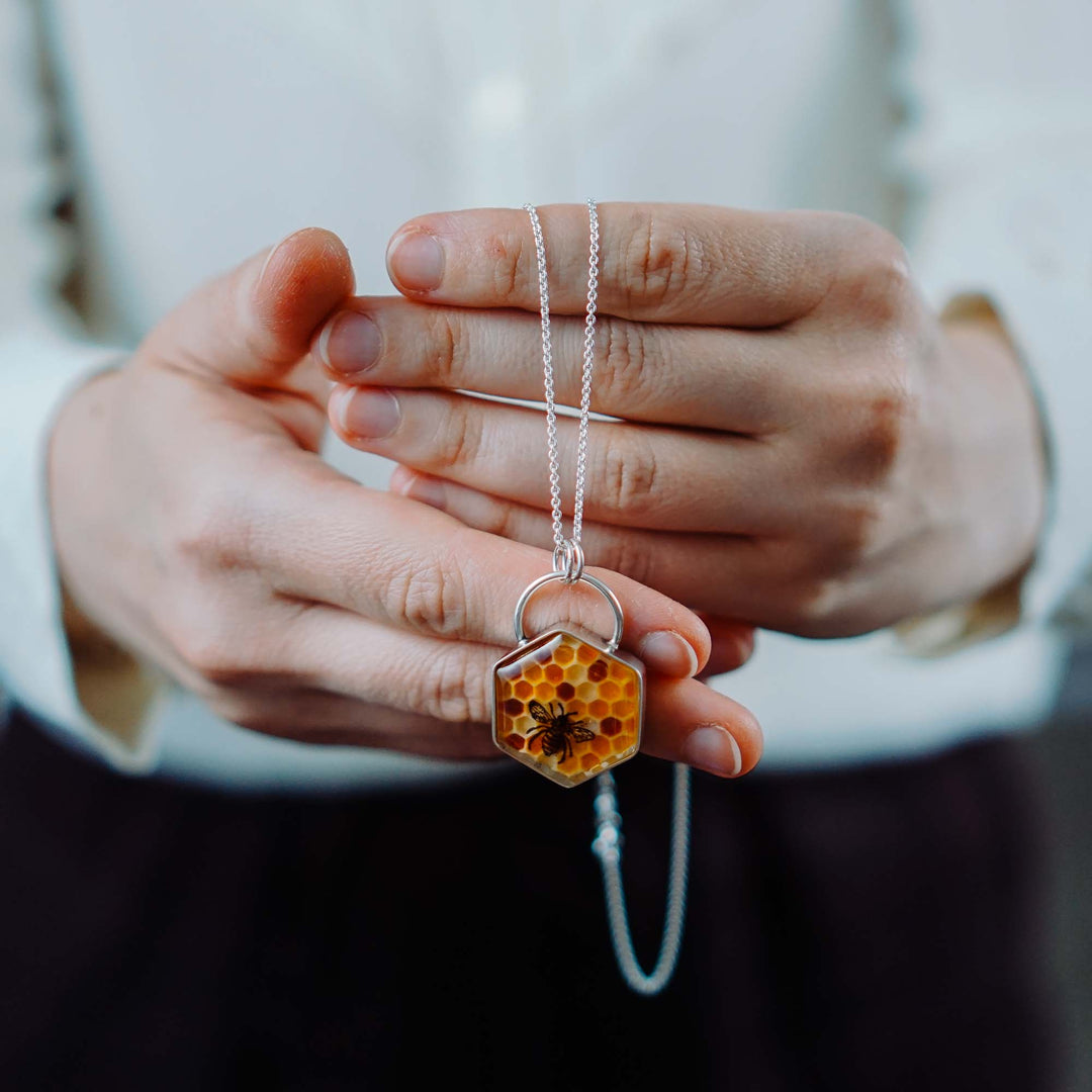 Kette aus Silber mit Honigwaben in gelb und orange mit einer schwarzen Biene. Die von Hand modellierte Honigwabe sitzt in einer silbernen Fassung aus 925 Sterling Silber. Die Rückseite des mittelgroßen Anhängers zieren ins Metall geschlagene Blumen und eine Biene.