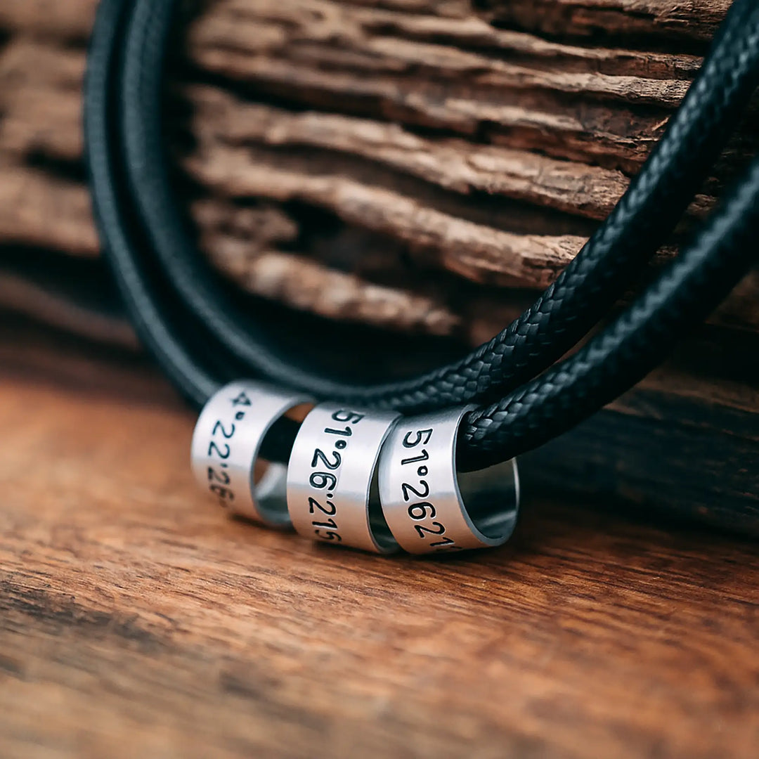 Eine vegane Halskette für Herren aus schwarzem Band, personalisiert mit Gravur von Koordinaten auf Sterling Silber 925 Perlen. Die Kette lässt sich mit einem Karabiner aus Edelstahl verschließen.