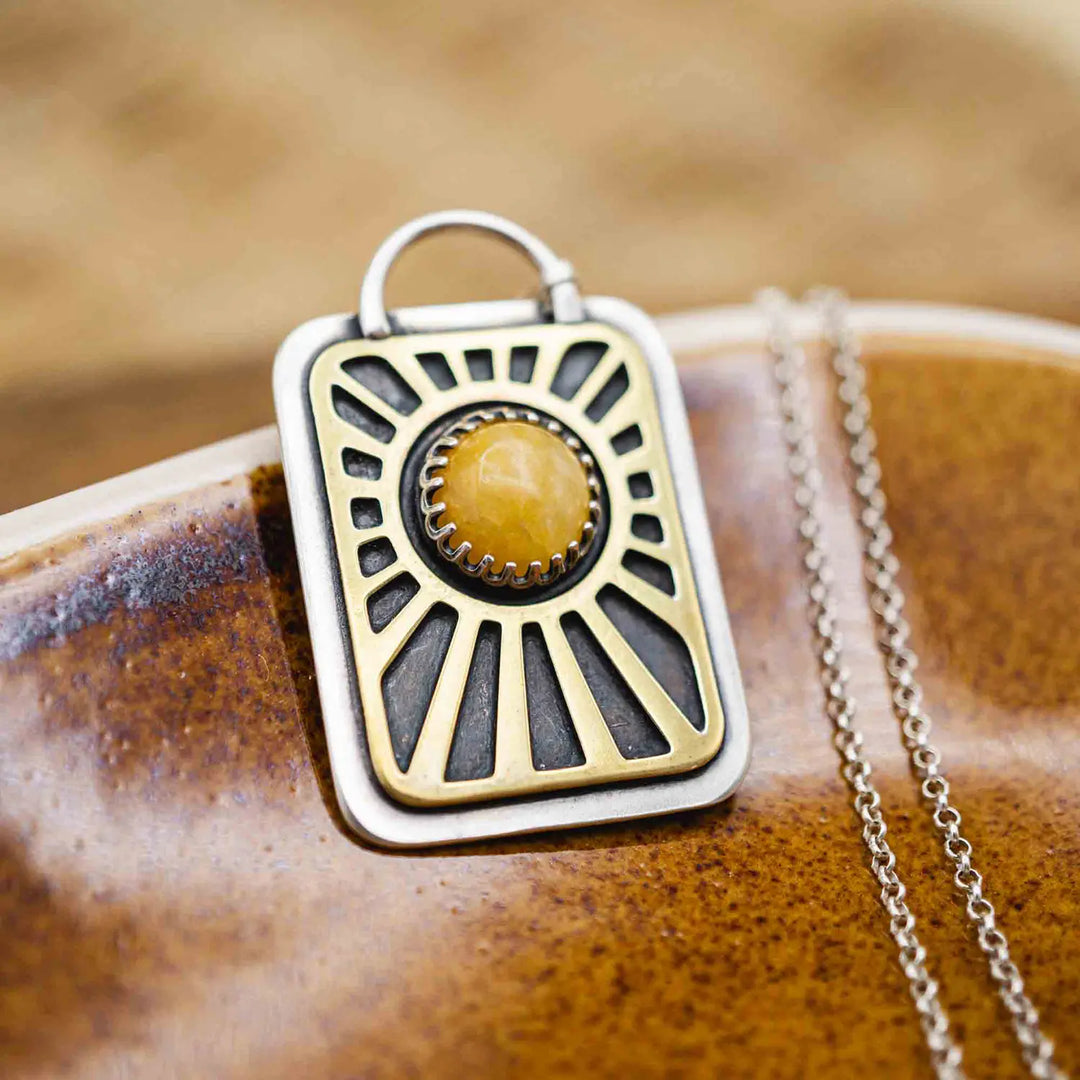 Kette aus Sterling Silber 925 mit gelbem Achat. Die handgefertigte Silberkette ist rechteckig und mit einer goldenen Sonne aus Messing versehen. In der Mitte der Sonne sitzt eingefasst in silberne Spitze, ein gelber Achat (Aventurin).
Auf der Rückseite des handgefertigten Silberschmucks ist zur Motivation eingraviert: "Alles unter der Sonne", um uns auch in schweren Zeiten zu erinnern, wie wertvoll das Leben ist.