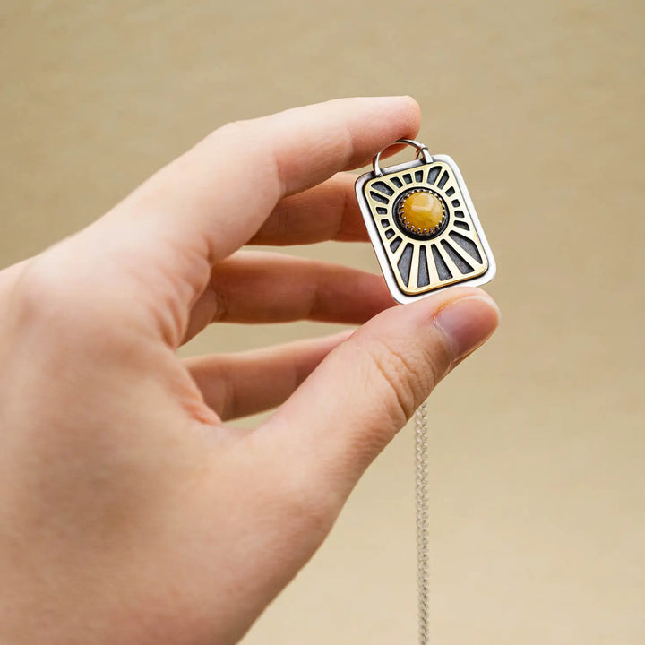 Kette aus Sterling Silber 925 mit gelbem Achat. Die handgefertigte Silberkette ist rechteckig und mit einer goldenen Sonne aus Messing versehen. In der Mitte der Sonne sitzt eingefasst in silberne Spitze, ein gelber Achat (Aventurin).
Auf der Rückseite des handgefertigten Silberschmucks ist zur Motivation eingraviert: "Alles unter der Sonne", um uns auch in schweren Zeiten zu erinnern, wie wertvoll das Leben ist.