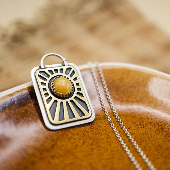 Kette aus Sterling Silber 925 mit gelbem Achat. Die handgefertigte Silberkette ist rechteckig und mit einer goldenen Sonne aus Messing versehen. In der Mitte der Sonne sitzt eingefasst in silberne Spitze, ein gelber Achat (Aventurin).
Auf der Rückseite des handgefertigten Sonnenanhängers ist zur Motivation eingraviert: "Alles unter der Sonne", um uns auch in schweren Zeiten zu erinnern, wie wertvoll das Leben ist.