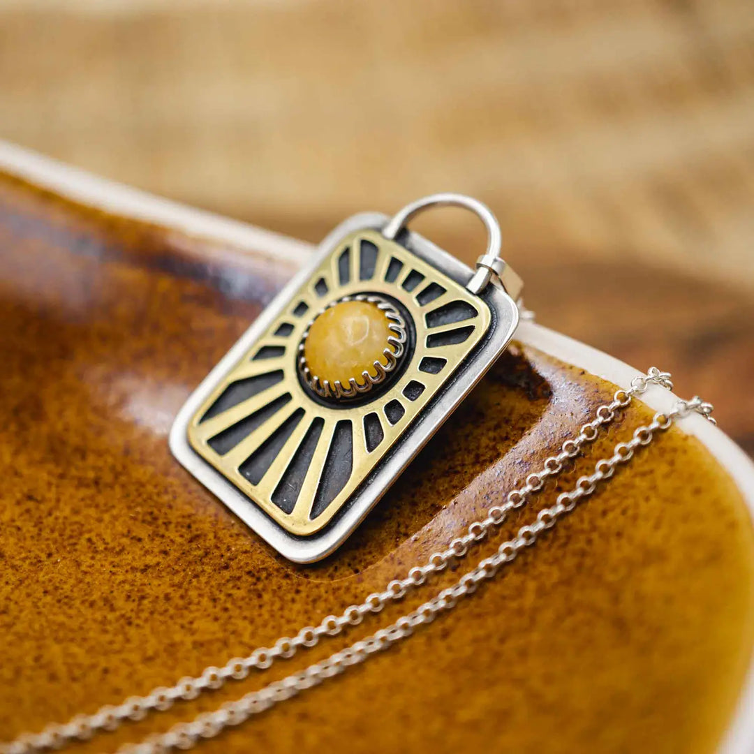Kette aus Sterling Silber 925 mit gelbem Achat. Die handgefertigte Silberkette ist rechteckig und mit einer goldenen Sonne aus Messing versehen. In der Mitte der Sonne sitzt eingefasst in silberne Spitze, ein gelber Achat (Aventurin).
Auf der Rückseite des handgefertigten Sonnenanhängers ist zur Motivation eingraviert: "Alles unter der Sonne", um uns auch in schweren Zeiten zu erinnern, wie wertvoll das Leben ist.