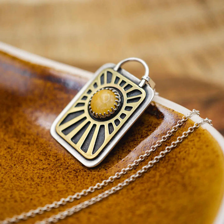 Kette aus Sterling Silber 925 mit gelbem Achat. Die handgefertigte Silberkette ist rechteckig und mit einer goldenen Sonne aus Messing versehen. In der Mitte der Sonne sitzt eingefasst in silberne Spitze, ein gelber Achat (Aventurin).
Auf der Rückseite des handgefertigten Sonnenanhängers ist zur Motivation eingraviert: "Alles unter der Sonne", um uns auch in schweren Zeiten zu erinnern, wie wertvoll das Leben ist.