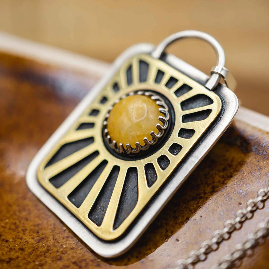 Kette aus Sterling Silber 925 mit gelbem Achat. Die handgefertigte Silberkette ist rechteckig und mit einer goldenen Sonne aus Messing versehen. In der Mitte der Sonne sitzt eingefasst in silberne Spitze, ein gelber Achat (Aventurin).
Auf der Rückseite des handgefertigten Sonnenanhängers ist zur Motivation eingraviert: "Alles unter der Sonne", um uns auch in schweren Zeiten zu erinnern, wie wertvoll das Leben ist.