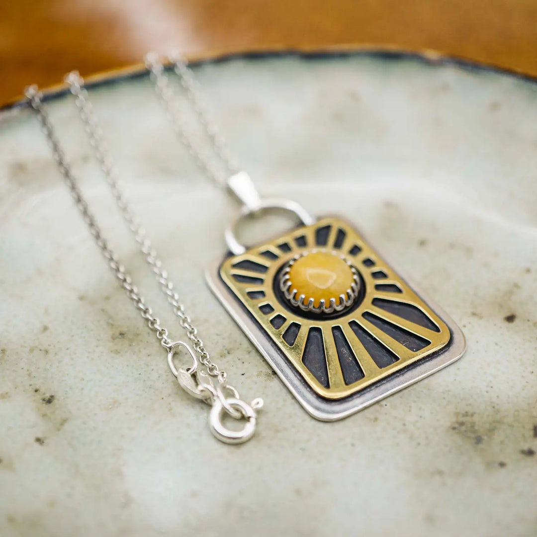 Kette aus Sterling Silber 925 mit gelbem Achat. Die handgefertigte Silberkette ist rechteckig und mit einer goldenen Sonne aus Messing versehen. In der Mitte der Sonne sitzt eingefasst in silberne Spitze, ein gelber Achat (Aventurin).
Auf der Rückseite des handgefertigten Sonnenanhängers ist zur Motivation eingraviert: "Alles unter der Sonne", um uns auch in schweren Zeiten zu erinnern, wie wertvoll das Leben ist.