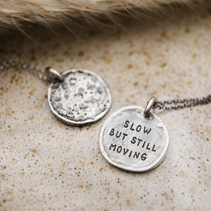 Runde Mond-Kette aus Sterling Silber 925 mit Gravur „Slow but still moving“ und strukturierter Rückseite im Hintergrund.