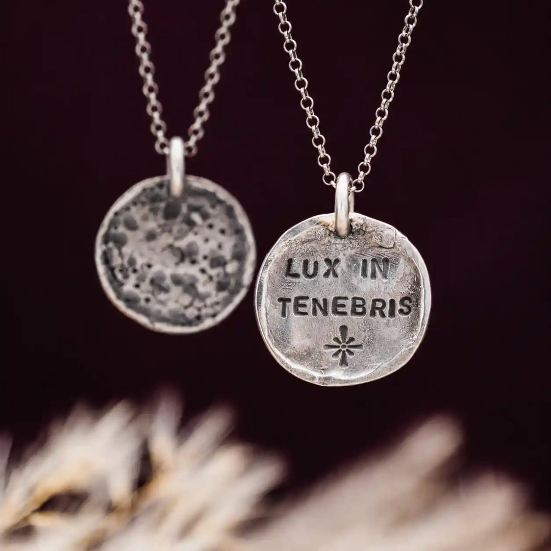 Handgemachte Mond-Ketten aus Silber 925 mit Gravur „Lux in Tenebris“ vor dunklem Hintergrund fotografiert.