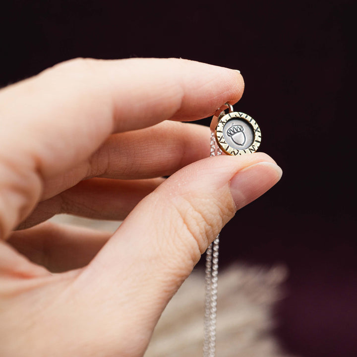 Eine kurze Silberkette aus Sterling Silber 925 mit einem kleinen gravierten Eichel Anhänger, eingerahmt von einem goldenem Rahmen.