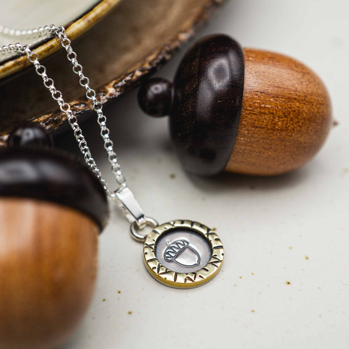 Eine kurze Silberkette aus Sterling Silber 925 mit einem kleinen gravierten Eichel Anhänger, eingerahmt von einem goldenem Rahmen.