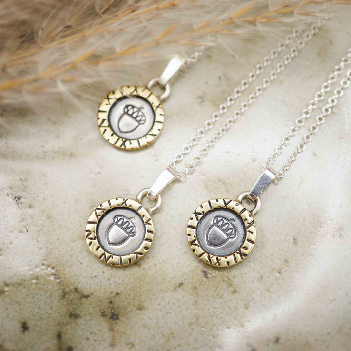 Eine kurze Silberkette aus Sterling Silber 925 mit einem kleinen gravierten Eichel Anhänger, eingerahmt von einem goldenem Rahmen.