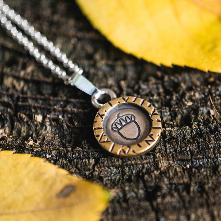 Eine kurze Silberkette aus Sterling Silber 925 mit einem kleinen gravierten Eichel Anhänger, eingerahmt von einem goldenem Rahmen.