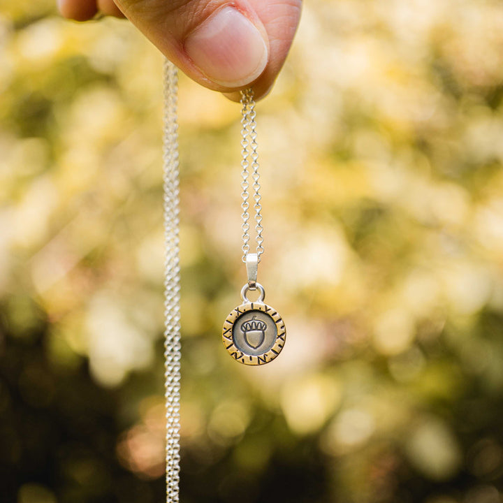 Eine kurze Silberkette aus Sterling Silber 925 mit einem kleinen gravierten Eichel Anhänger, eingerahmt von einem goldenem Rahmen.